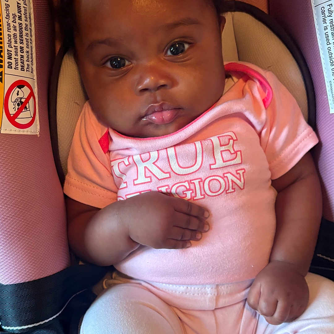 Quinnari is registered to the contest to win money with this photo: baby, child, infant, car_seat, pink_clothing, bows, hair_accessories, cute, portrait, sitting, indoors, young_child, looking, face, closeup, clothing, footwear, sock, hand, expression
