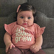 Mia joined the competition — help win amazing prizes! baby, infant, child, cute, pink_clothing, hair_clip, sitting, couch, gray_couch, indoor, portrait, face, eyes, hands, legs, toddler, expression, person, apparel, comfortable