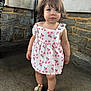 toddler, child, girl, floral_dress, sandals, stone_wall, concrete_floor, standing, outdoor, curly_hair, cute, portrait, person, casual_clothing, summer, innocent, young, fashion, footwear, expression