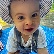 Mylian a rejoint le concours — aidez-le/la à gagner de superbes lots ! toddler, child, smile, hat, striped_hat, overalls, outdoor, daylight, picnic, blue_blanket, grass, hand, holding_hand, happy, face, eyes, baby, person, clothing, nature