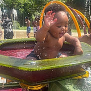 Malano is registered to the contest to win money with this photo: child, toddler, water, splashing, playground, outdoor, summer, sunlight, water_park, fun, happy, people, water_spray, greenery, play, swimwear, daytime, recreation, park, activity