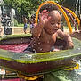 child, toddler, water, splashing, playground, outdoor, summer, sunlight, water_park, fun, happy, people, water_spray, greenery, play, swimwear, daytime, recreation, park, activity