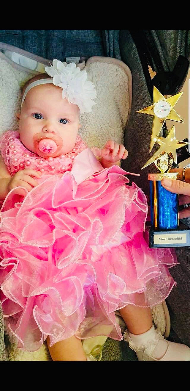 Harper is registered to the contest to win money with this photo: baby, baby_toddler_clothing, cheek, child, costume, dress, fashion_accessory, hair_accessory, headgear, peach, person, pink, product, skin, smile, textile, toddler