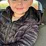 child, boy, smile, blue_eyes, puffer_jacket, black_jacket, car_interior, seat, window, outdoor_background, nature, greenery, orange_flowers, portrait, happy, casual_clothing, young, person, face, head