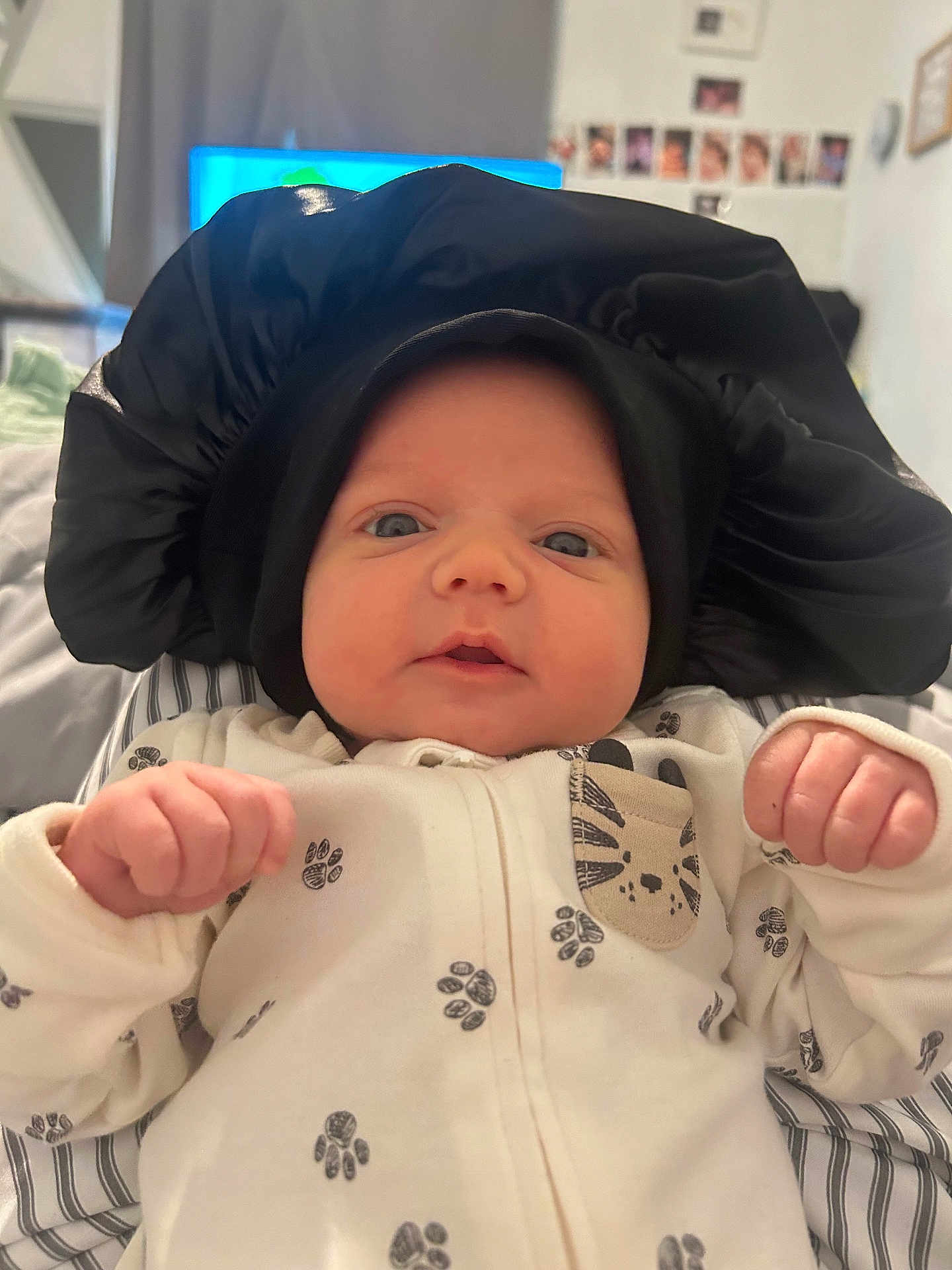 Axl joined the competition — help win amazing prizes! baby, infant, face, black_bonnet, onesie, paw_prints, fist, blue_eyes, indoor, bed, blanket, curious, cute, portrait, child, newborn, clothing, soft_lighting, closeup, headwear