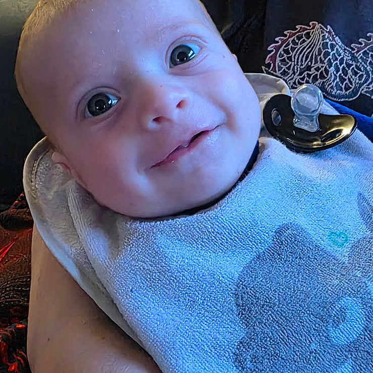 Leo a rejoint le concours — aidez-le/la à gagner de superbes lots ! arm, baby, bib, closeup, cloth, cute, expression, eyes, face, furniture, hand, holding, indoor, infant, kitchen, pacifier, person, portrait, smiling, toddler