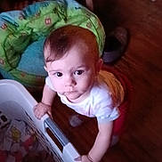 Nova joined the competition — help win amazing prizes! baby, child, laundry_basket, indoor, floor, toy, curious, standing, looking_up, furniture, clothing, wood_floor, green_cushion, white_shirt, red_pants, person, home, play_area, infant, expression