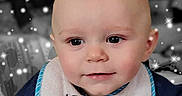 Legend is registered to the contest to win money with this photo: baby, child, bib, face, smile, sparkles, blue_clothing, closeup, infant, cute, portrait, hand, eyes, skin, head, sitting, young_child, expression, background_blur, indoor