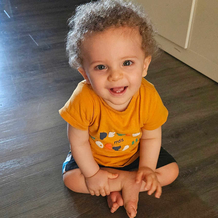 Morgann participe au concours pour gagner de l'argent avec cette photo : baby, bodypart, clothing, crawling, face, finger, hand, happy, hardwood, head, indoors, interiordesign, pants, person, photography, portrait, sitting, smile, t_shirt, wood