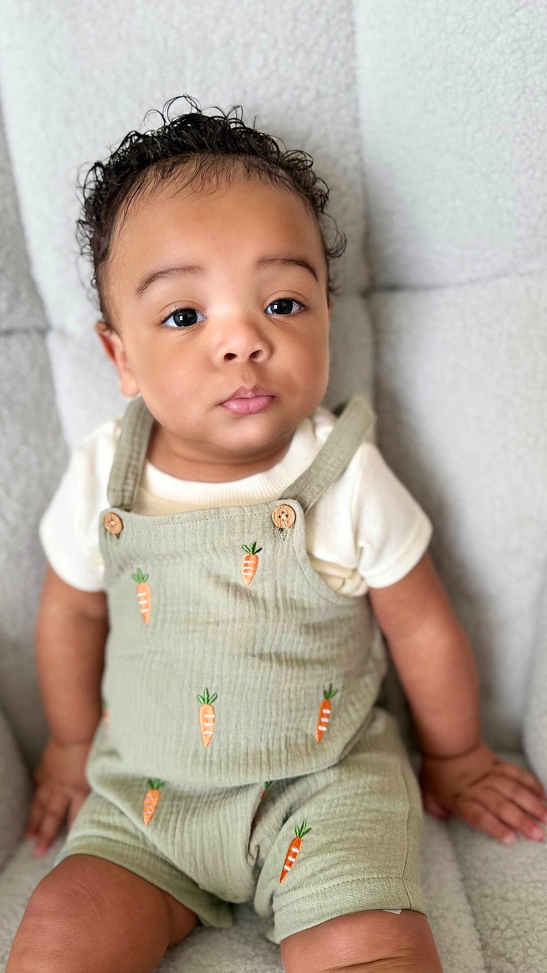 Rogelio is registered to the contest to win money with this photo: baby, child, curly_hair, romper, carrot_pattern, cute, sitting, indoors, portrait, cozy, comfortable, curious, clothing, person, infant, soft_texture, closeup, face, hands, light