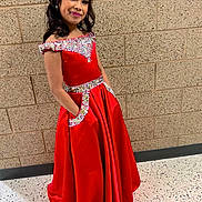 Avyannah is registered to the contest to win money with this photo: child, girl, red_dress, formal_dress, sparkles, embellishment, long_hair, makeup, smile, pose, brick_wall, hallway, tile_floor, pocket, portrait, elegant, pageant, young_person, standing, fashion