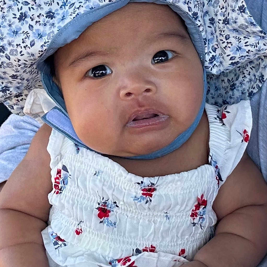 Aila is registered to the contest to win money with this photo: accessories, baby, bonnet, cap, clothing, dress, face, frown, hat, head, jewelry, necklace, newborn, person, photography, portrait, sad, sitting, sunhat, t_shirt