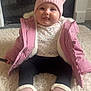 Emmie is registered to the contest to win money with this photo: baby, child, pink_jacket, hat, pom_poms, boots, sitting, carpet, indoor, cute, tongue_out, warm_clothing, smiling, face, person, fur_lining, floor, cozy, winter_wear, portrait