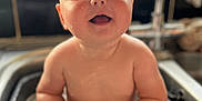 Emmie is registered to the contest to win money with this photo: baby, sink, water, container, smile, happy, kitchen, child, cute, sitting, naked, playful, face, blue_eyes, chubby, indoors, clean, wet, young, curious