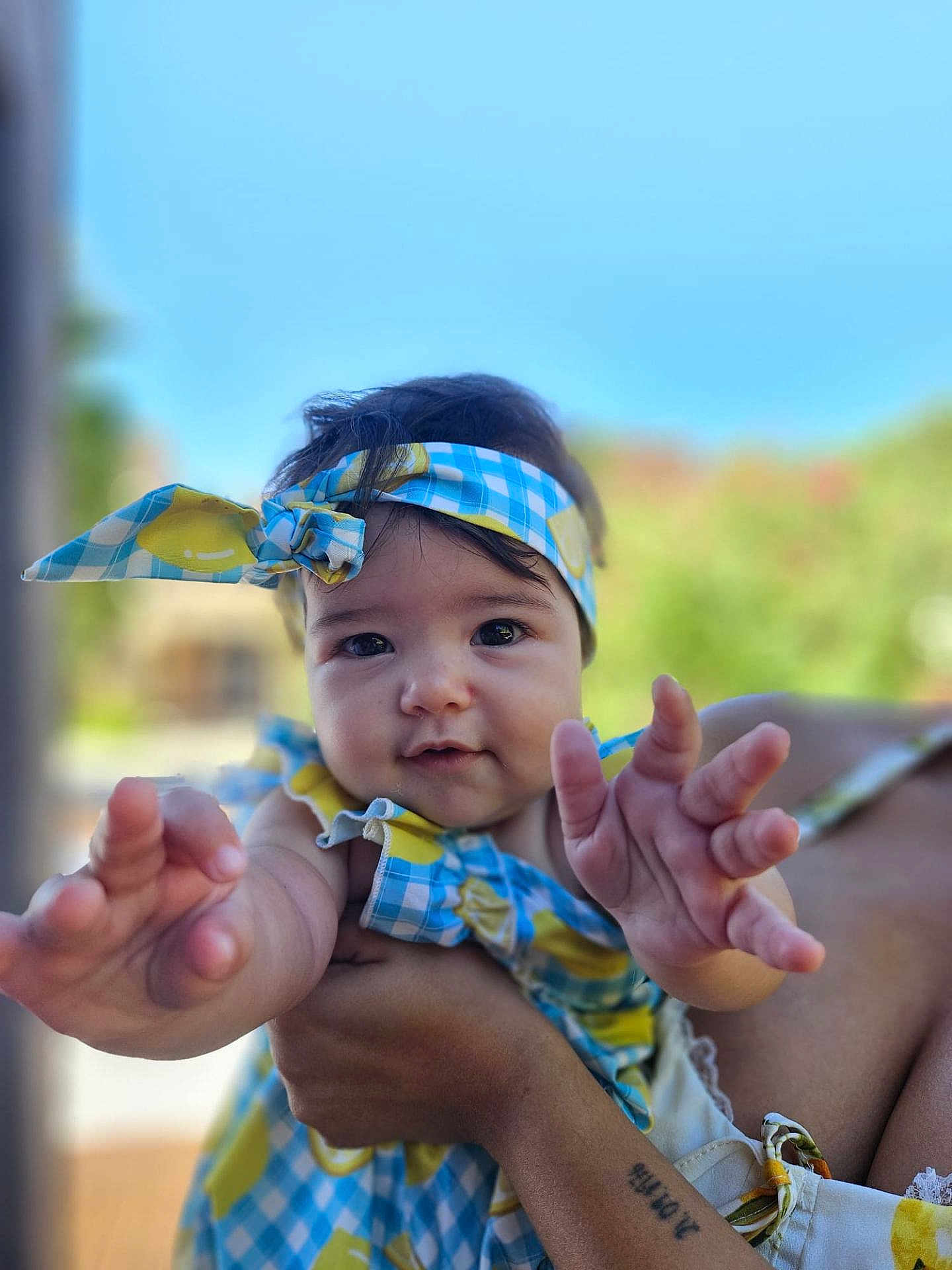 Emma a rejoint le concours — aidez-le/la à gagner de superbes lots ! baby, child, headband, blue_sky, outdoor, hand, person, smiling, portrait, tattoo, clothing, cute, skin, face, arm, holding, summer, daylight, cheerful, infant