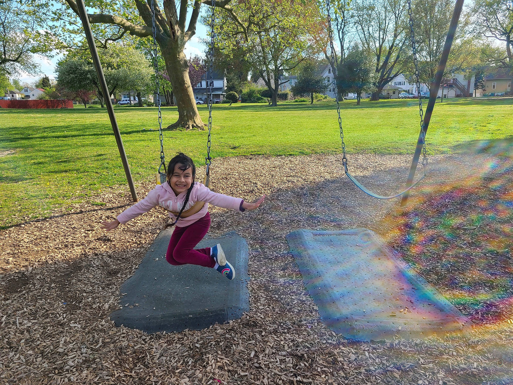 Sara is registered to the contest to win money with this photo: botany, city, fun, grass, happy, joy, leaf, leisure, outdoor_play_equipment, people_in_nature, person, plant, playground, recreation, shade, sitting, sky, soil, swing, tree