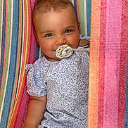 Adèle a rejoint le concours — aidez-le/la à gagner de superbes lots ! baby, pacifier, smiling, striped_hammock, colorful, floral_shirt, short_sleeves, child, cute, portrait, relaxed, outdoor, infant, happy, person, clothing, fabric, pattern, closeup, skin