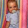 baby, pacifier, smiling, striped_hammock, colorful, floral_shirt, short_sleeves, child, cute, portrait, relaxed, outdoor, infant, happy, person, clothing, fabric, pattern, closeup, skin