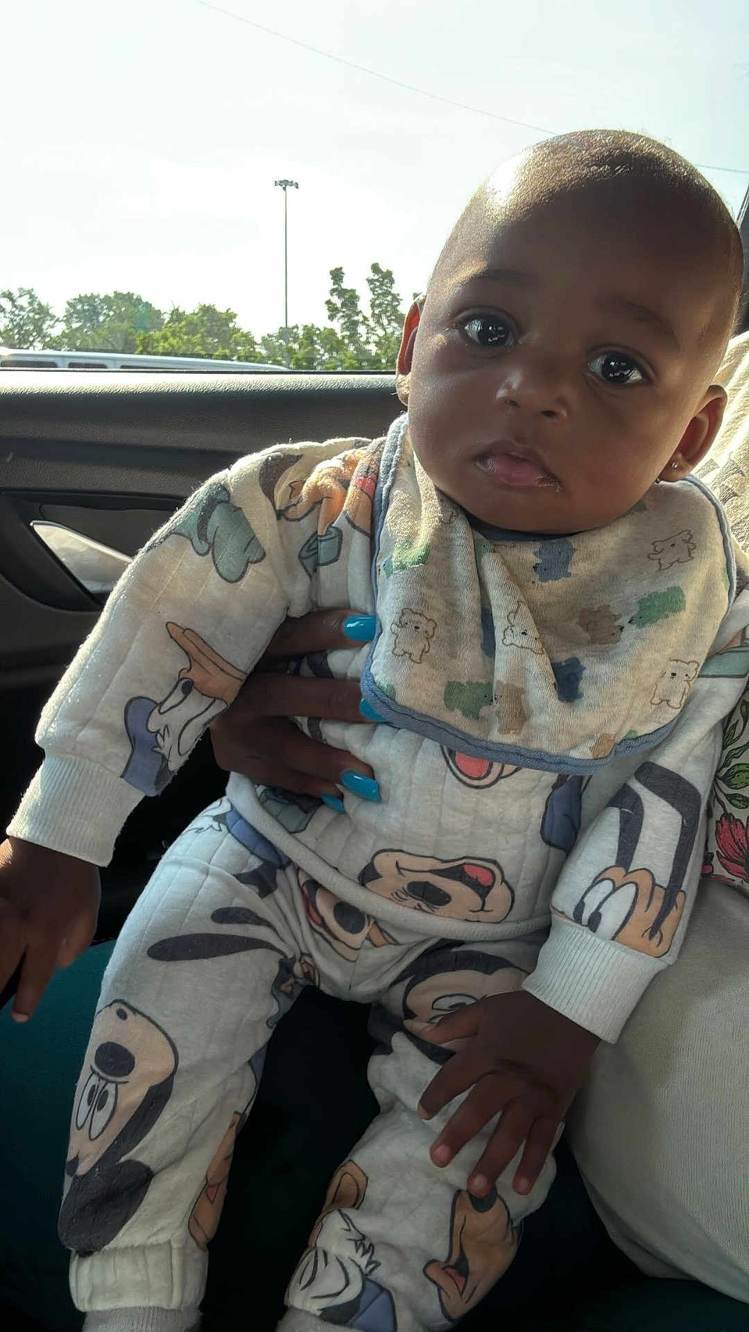 Iyon joined the competition — help win amazing prizes! baby, child, infant, cartoon_clothing, car_interior, hand, blue_nail_polish, window, trees, light_pole, curious_look, cozy_outfit, bib, long_sleeves, pants, sitting, portrait, dark_skin, indoor, daylight
