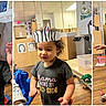 activity_table, background_poster, braided_hair, child, classroom, crafting, curly_hair, indoor, paper_crown, paper_hat, playroom, smiling, text_on_shirt, toddler, toy_car, toys, tshirt, two_children, wooden_chair, wooden_floor