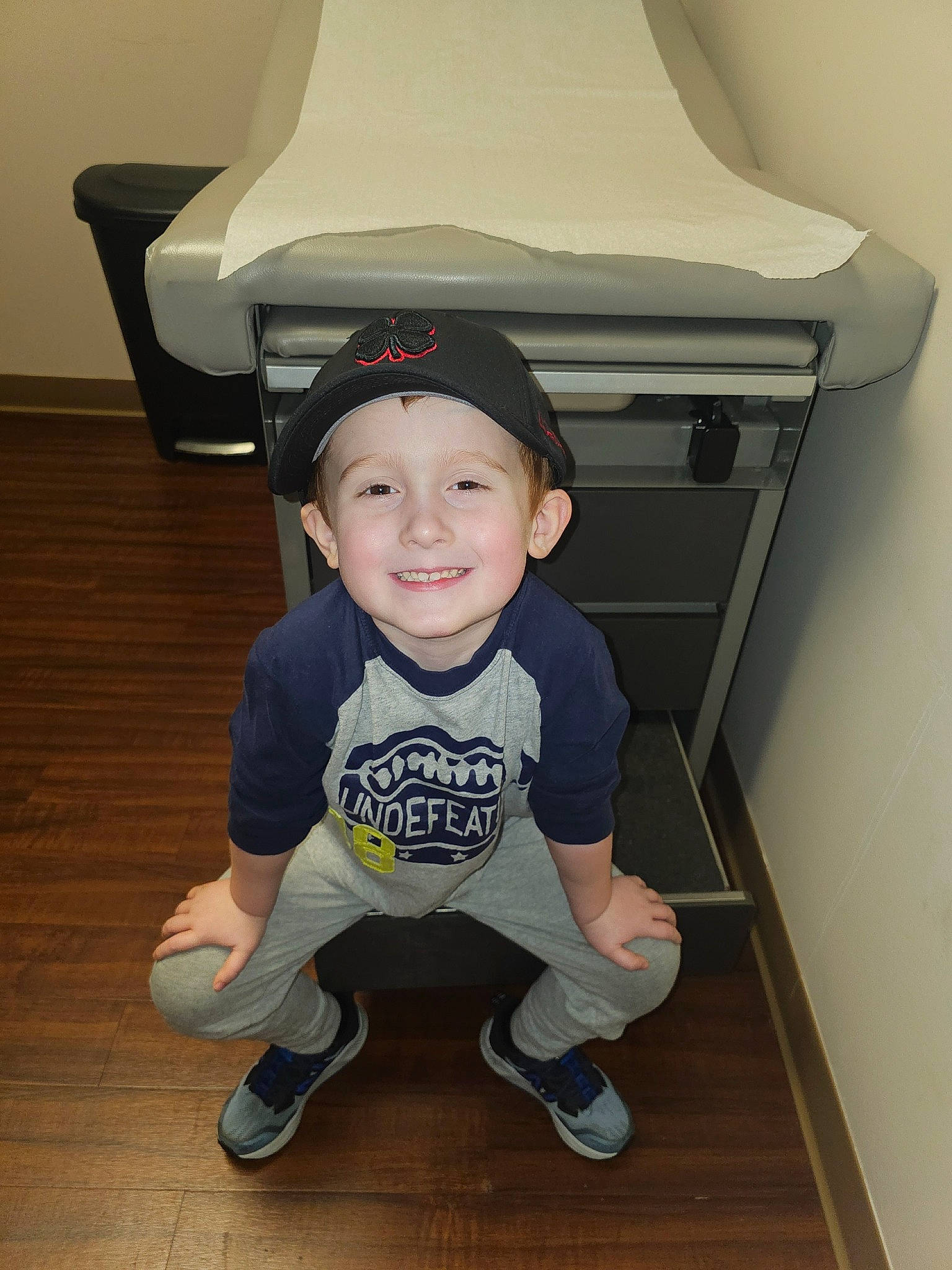 Zane is registered to the contest to win money with this photo: baby_toddler_clothing, child, comfort, face, flooring, happy, hardwood, hat, head, headwear, joy, knee, person, shoe, sitting, sleeve, smile, sneakers, sportswear, t_shirt