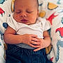 baby, sleeping, infant, onesie, denim_pants, hands, blanket, dinosaur_pattern, peaceful, closeup, portrait, child, cute, soft_light, indoor, newborn, resting, calm, relaxed, skin
