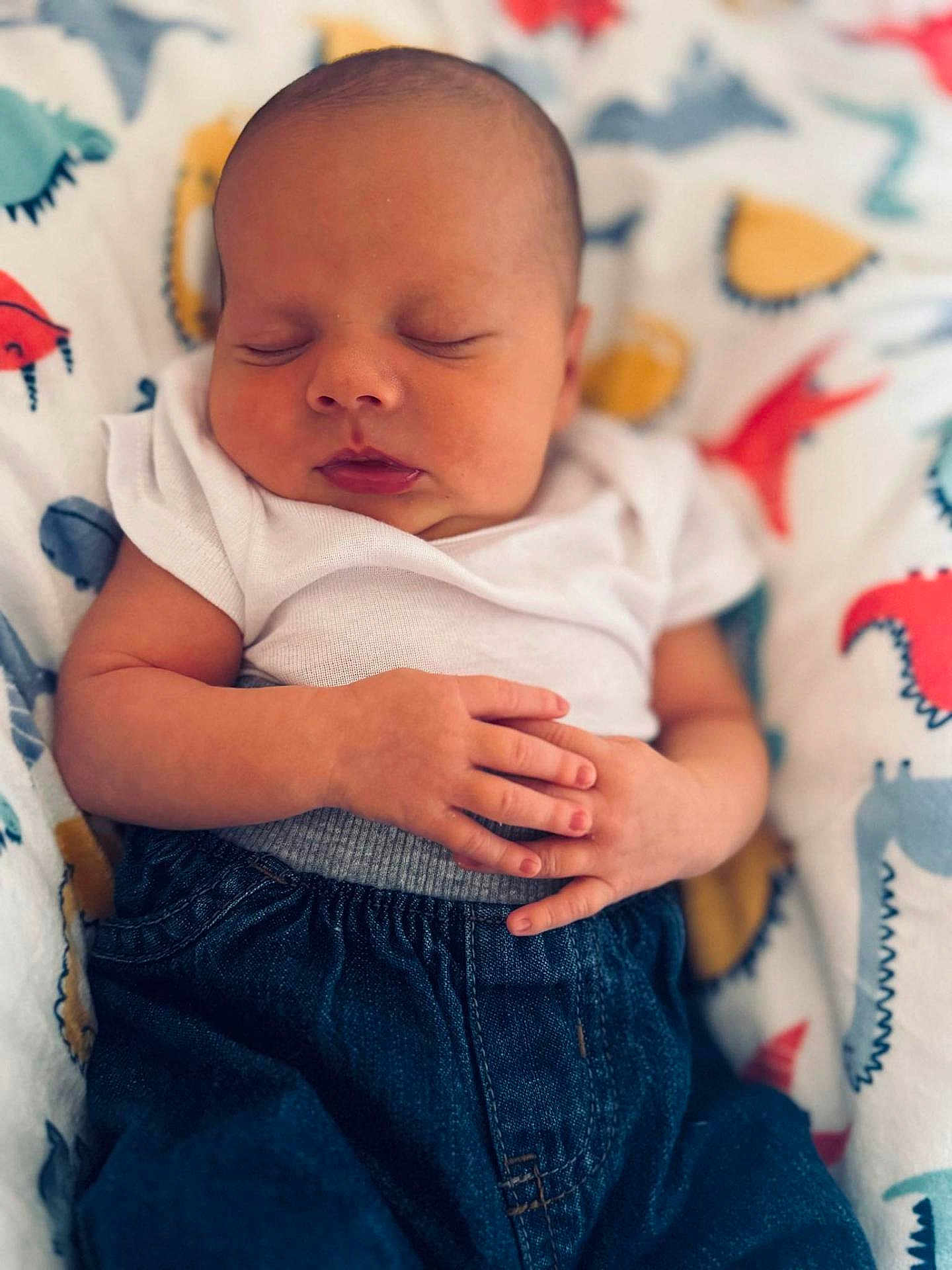 Caspiayn is registered to the contest to win money with this photo: baby, sleeping, infant, onesie, denim_pants, hands, blanket, dinosaur_pattern, peaceful, closeup, portrait, child, cute, soft_light, indoor, newborn, resting, calm, relaxed, skin