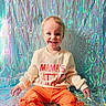 toddler, child, smiling, sweater, orange_pants, bows, holographic_background, sitting, happy, portrait, indoor, colorful, cute, fashion, young_child, playful, clothing, face, person, bright