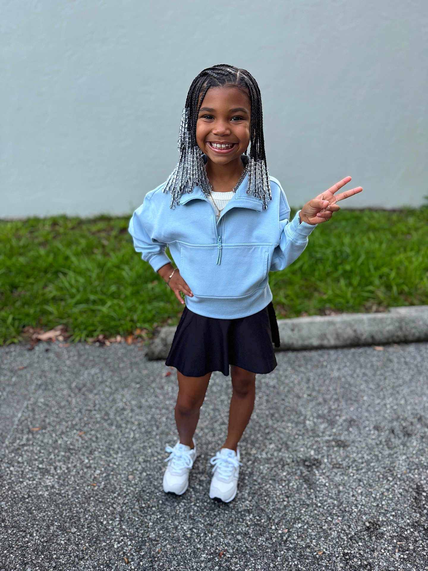 K Couture joined the competition — help win amazing prizes! child, girl, smiling, peace_sign, braids, beads, blue_sweater, black_skirt, white_sneakers, outdoor, sidewalk, grass, wall, happy, standing, casual_clothing, portrait, person, fashion, youth