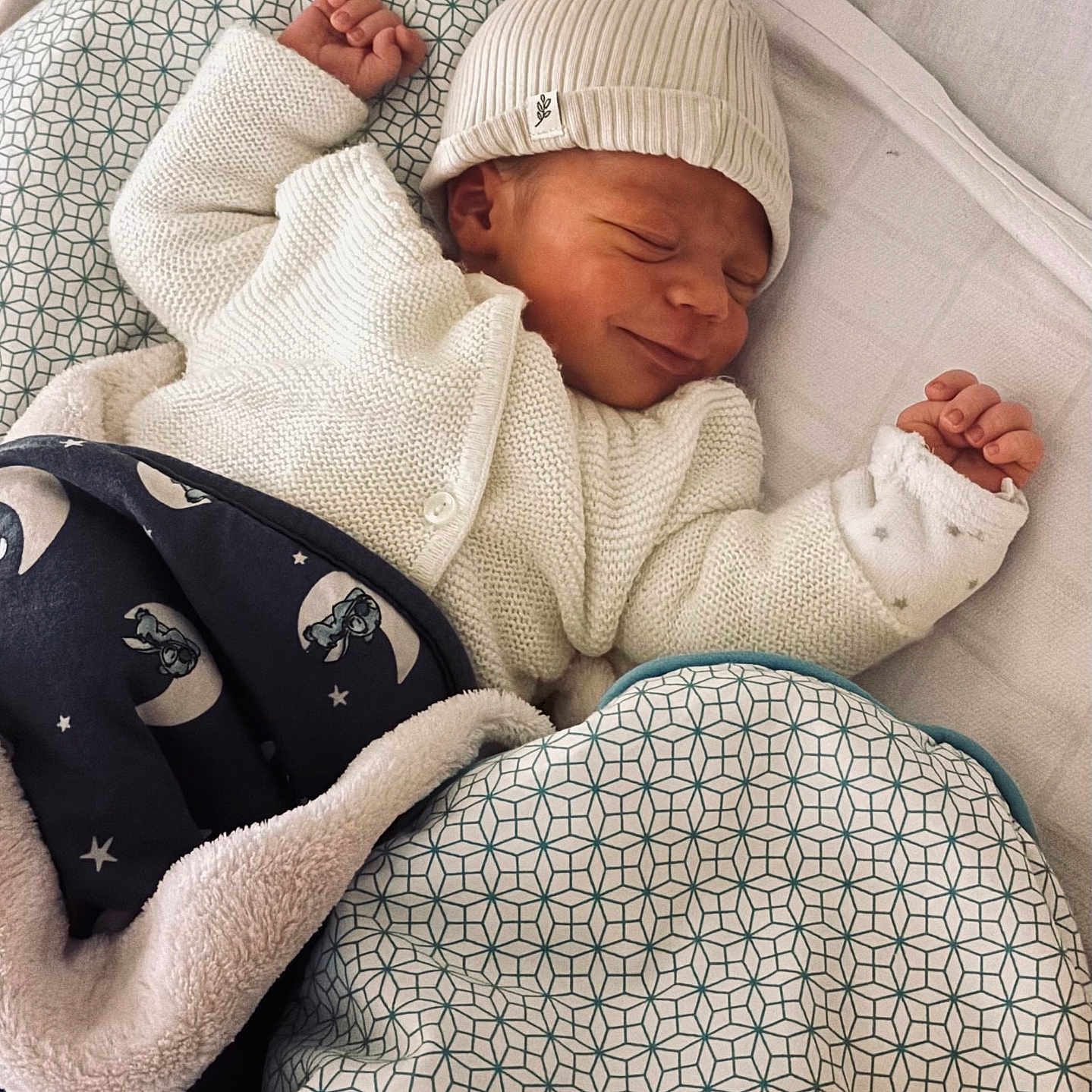 Karel participe au concours pour gagner de l'argent avec cette photo : baby, beanie, bed, blanket, cozy, crib, infant, knit_cardigan, moon_pattern, newborn, nursery, patterned_blanket, pillow, plush_toy, portrait, sleeping, smile, soft_texture, swaddle, tiny_hands
