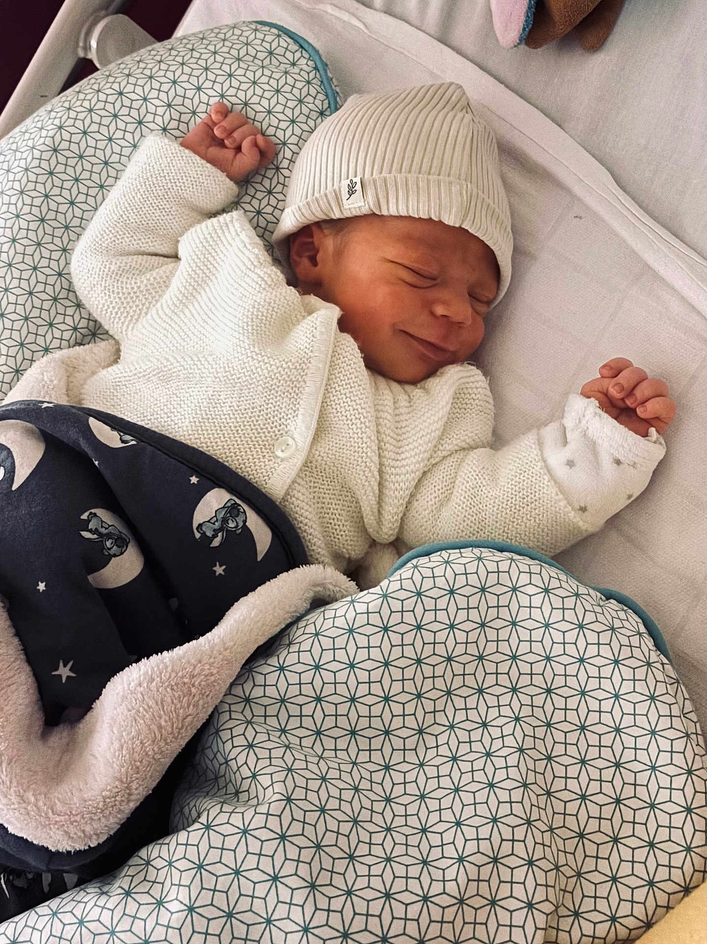 Karel participe au concours pour gagner de l'argent avec cette photo : baby, newborn, infant, sleeping, smile, beanie, knit_cardigan, blanket, patterned_blanket, pillow, crib, swaddle, tiny_hands, plush_toy, cozy, portrait, soft_texture, nursery, moon_pattern, bed