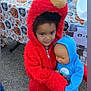 Paislee is registered to the contest to win money with this photo: child, costume, elmo, doll, baby_doll, halloween, pumpkin_tablecloth, table, bowl, outdoor, pavement, hood, red_fur, cute, smile, holding, people, toy, portrait, event
