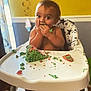 child, baby, toddler, highchair, cake, green_frosting, mess, eating, hands, face, wide_eyes, brown_hair, socks, tray, party_decor, streamers, indoor, celebration, cheeky_expression, crumbs
