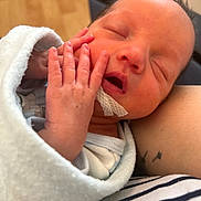 Henslee is registered to the contest to win money with this photo: newborn, baby, infant, sleeping, blanket, swaddle, hand, fingers, face, mouth_open, nose, eyelids, skin, medical_tape, tattoo, arm, striped_clothing, closeup, portrait, wood_floor