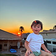 Ozias joined the competition — help win amazing prizes! toddler, child, white_tshirt, green_shorts, sunset, concrete_wall, supporting_hands, suburban, house, backyard, outdoor, evening, sky, palm_tree, person, casual_clothing, cute, expression, family, playful
