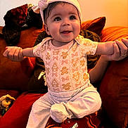 Riley is registered to the contest to win money with this photo: baby, child, headband, smiling, person, couch, cushion, orange, red, clothing, sitting, happy, indoors, portrait, infant, hand, holding, cute, cozy, warm_lighting