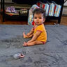Riley joined the competition — help win amazing prizes! baby, child, indoor, carpet, yellow_onesie, pacifier, diapers, shelf, purple_slippers, wooden_floor, curly_hair, looking_at_camera, sitting, floor, home, infant, cute, person, young_child, playtime