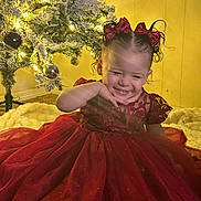 Yasely joined the competition — help win amazing prizes! child, toddler, girl, red_dress, bow, holiday, christmas_tree, ornament, lights, smile, happy, indoor, portrait, curly_hair, sitting, plush_rug, festive, sparkle, wall, photography