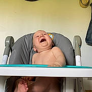 Ayden a rejoint le concours — aidez-le/la à gagner de superbes lots ! baby, high_chair, laughing, indoor, child, bare_skin, face, foot, hand, toy, clock, wall, hat, seat, furniture, diaper, smile, happy, person, home