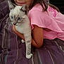 child, cat, bedspread, striped, pink_shirt, hugging, indoor, feline, pet, curious, young, blue_eyes, soft_focus, comfort, cozy, striped_bed, animal, domestic, resting, cuddle