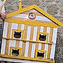 Tigrou participe au concours pour gagner de l'argent avec cette photo : wooden_cat_house, cat_silhouettes, yellow_paint, white_paint, stone_wall, wooden_pallet, cat, animal_shelter, outdoor, person_arm, window_cutouts, pet_house, four_windows, animal_silhouette, yellow_trim, wooden_structure, animal_housing, daylight, partial_person, rustic