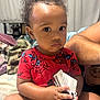 toddler, child, indoor, person, red_shirt, spiderman, cards, curly_hair, earring, diaper, blanket, bed, arm, expression, holding, sitting, face, clothing, home, curious