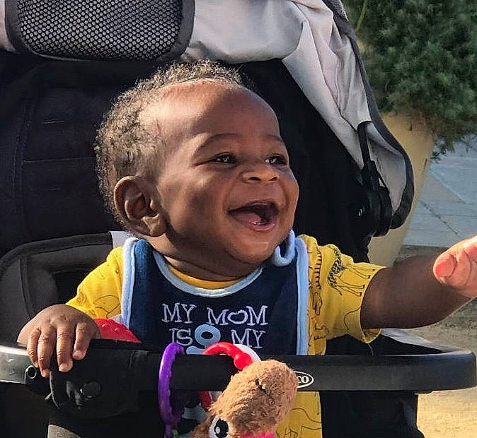 Cassidy is registered to the contest to win money with this photo: baby_carriage, baby_products, child, cool, finger, fun, gesture, hand, happy, mammal, mouth, organ, person, sleeve, smile, t_shirt, thumb, toddler, travel, tree