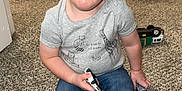 Everitt is registered to the contest to win money with this photo: toddler, child, barefoot, carpet, toy_car, jeans, gray_shirt, indoor, home, curious, sitting, carpeted_floor, short_hair, blue_eyes, casual_clothing, playing, expression, young_child, person, floor_vent