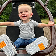 Everitt is registered to the contest to win money with this photo: toddler, child, swing, smiling, outdoor, playground, happy, jeans, sneakers, short_sleeve_shirt, animal_print, nature, greenery, park, fun, joy, arms_outstretched, seat, play, daylight