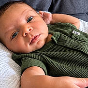 Jalen is registered to the contest to win money with this photo: baby, infant, child, portrait, lying_down, green_outfit, romper, bed, blanket, cushion, indoor, close_up, face, eyes, wide_eyed, calm, cute, skin, photography, soft_lighting