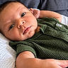 baby, infant, child, portrait, lying_down, green_outfit, romper, bed, blanket, cushion, indoor, close_up, face, eyes, wide_eyed, calm, cute, skin, photography, soft_lighting