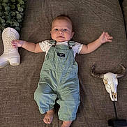Micah is registered to the contest to win money with this photo: baby, baby_lying_down, brown_couch, child, couch, cowboy_boot, cute_baby, decorative_skull, face, footwear, green_overalls, home_decor, horns, indoor, infant, overalls, plant_leaves, portrait, smiling_baby, western_style
