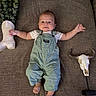 baby, baby_lying_down, brown_couch, child, couch, cowboy_boot, cute_baby, decorative_skull, face, footwear, green_overalls, home_decor, horns, indoor, infant, overalls, plant_leaves, portrait, smiling_baby, western_style