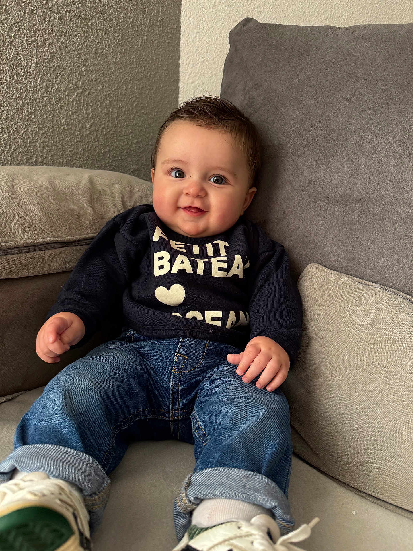 Gabriel participe au concours pour gagner de l'argent avec cette photo : baby, child, smiling, jeans, sneakers, sitting, couch, sweater, indoor, cozy, cute, portrait, happy, casual_clothing, young_child, furniture, home, comfortable, person, face